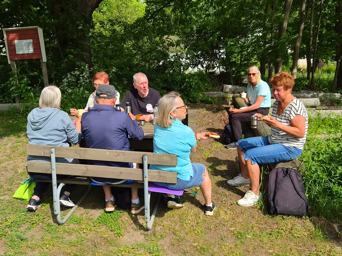 Personer sitter runt ett bord och äter medhavd matsäck.