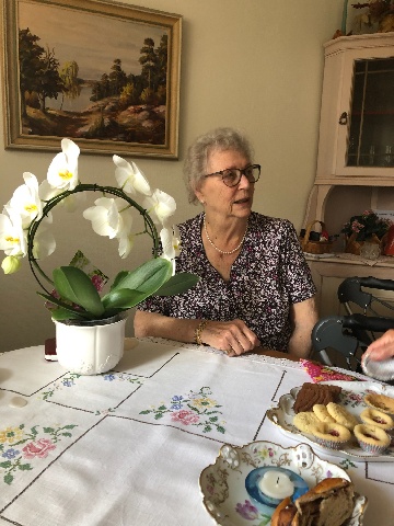 Kvinna vid ett bord dukat med blommor och fika.