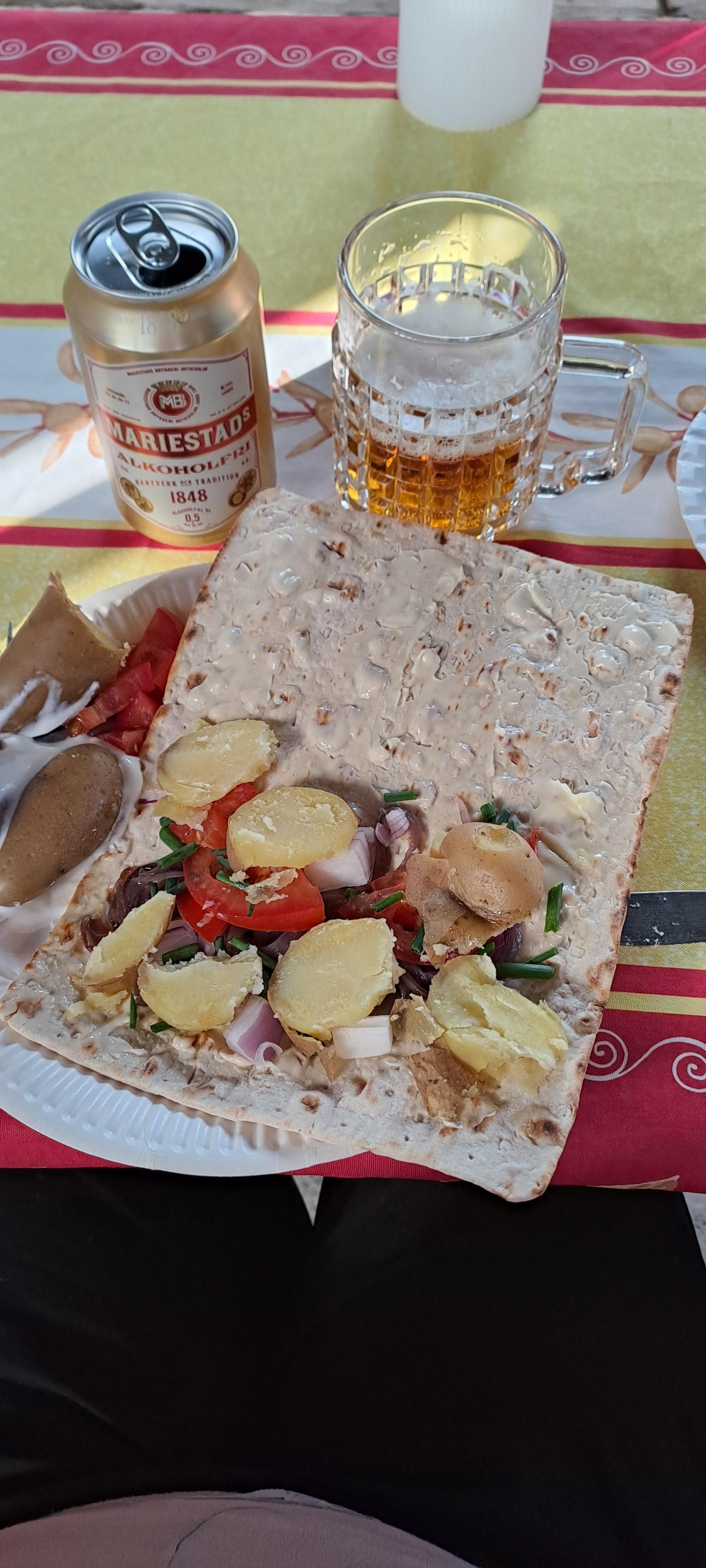Hårt bröd med surströmming och diverse tillbehör på samt en burk öl och ett glas med öl i.
