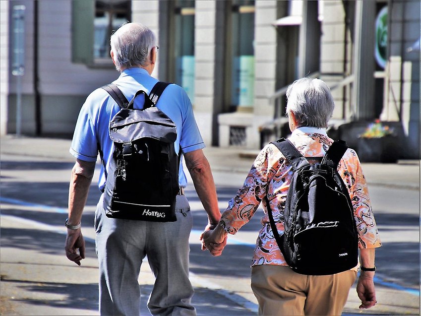 Två äldre pensioner går hand i hand på en gata.