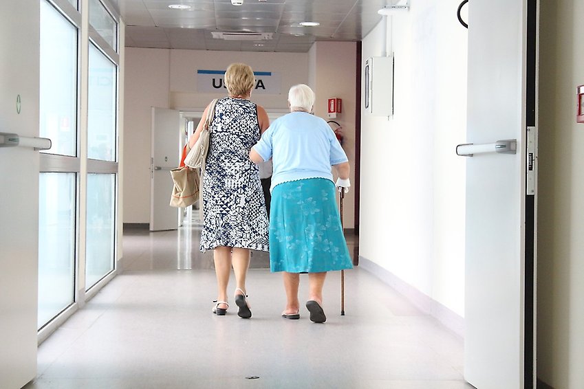 En pensionärer får stöd av en anhörig i en korridor.