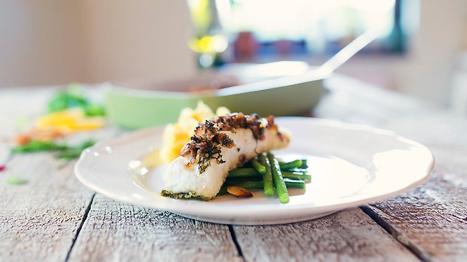En vit porslinstallrik med fisk och grönsaker på.