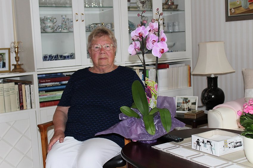 En kvinna sitter vid ett bord och på bordet står en orkidé.