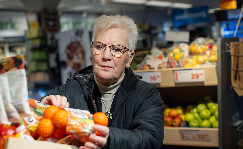 En äldre kvinna i en matbutik tittar på prislappen på en påse apelsiner.