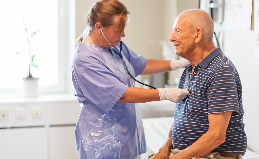 En läkare lägger ett stetoskop mot bröstet på en äldre manlig patient.