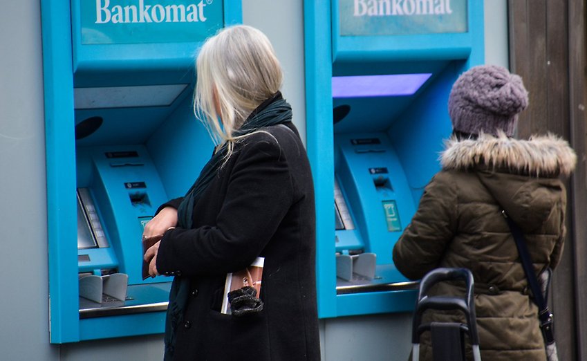 Två kvinnor står vid varsin bankomat.