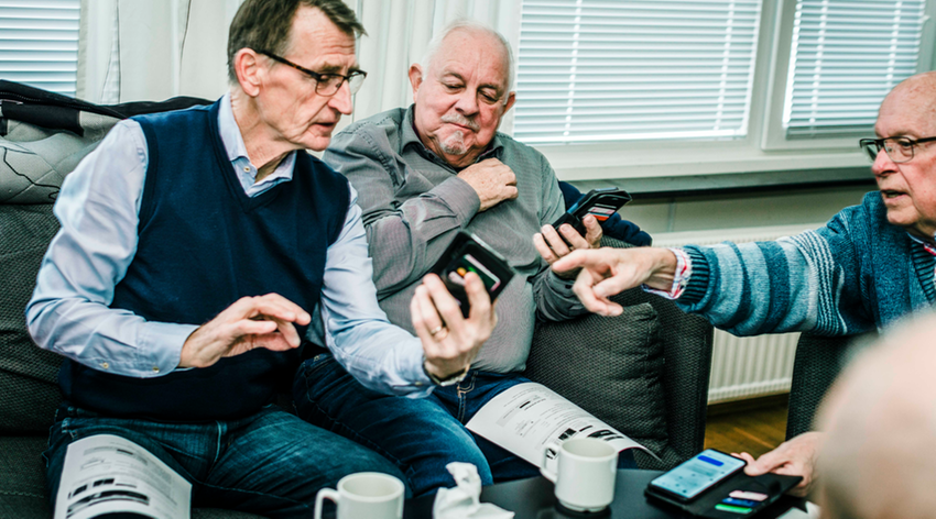 Tre män som tittar på mobiltelefoner och diskuterar