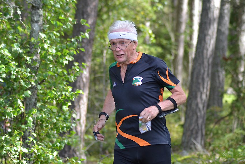 En äldre man i orienteringskläder springer med en karta i vänster hand.