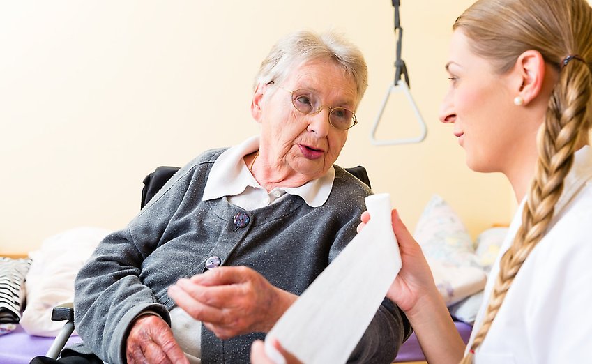 En äldre kvinna samtalar med en sköterska i blå arbetskläder.