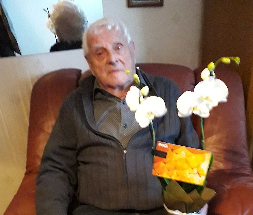 En man som sitter i e i sin hand.n stol håller en blommande krukväxt