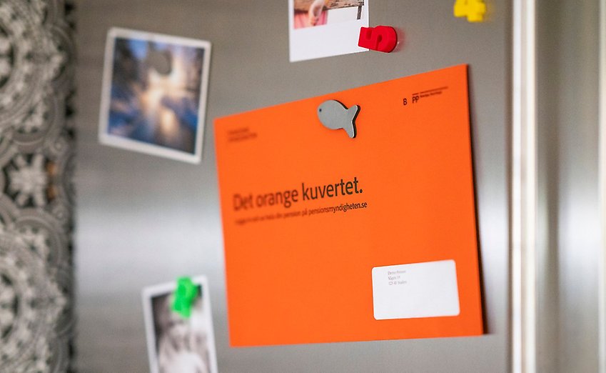 Det orangea kuvertet från Pensionsmyndigheten uppsatt med magneter på ett silvergrått kylskåp.